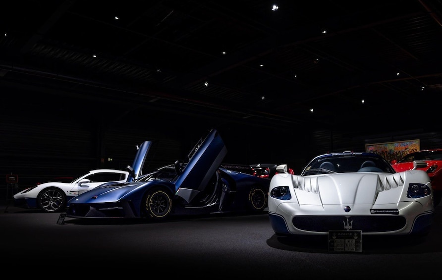 Three luxury sports cars displayed in a dimly lit indoor setting. 1