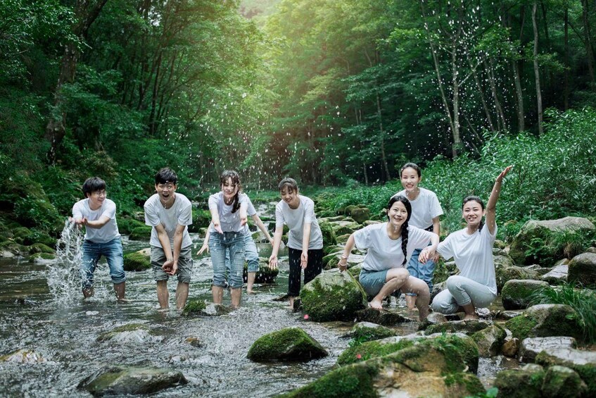 A group of people playing in a forest stream surrounded by rocks and greenery. 2