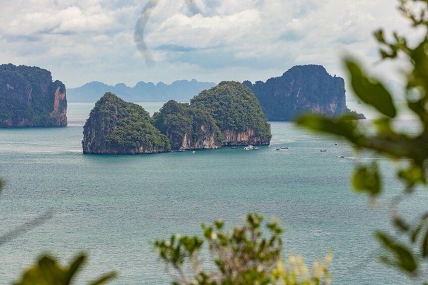 A calm sea with several small islands, one with dense greenery, and distant rocky formations under a cloudy sky. 4
