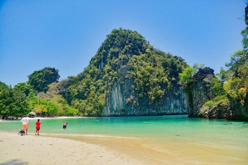 A beach with clear turquoise water, a large green mountain, and a few people walking. 4