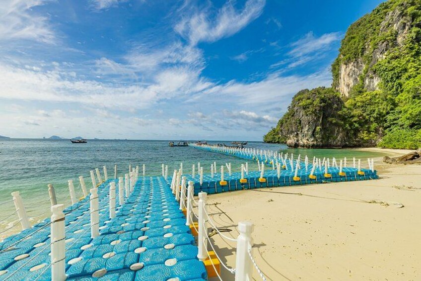 A beach with a blue and white floating barrier, clear blue sky, and a rocky cliff. 2