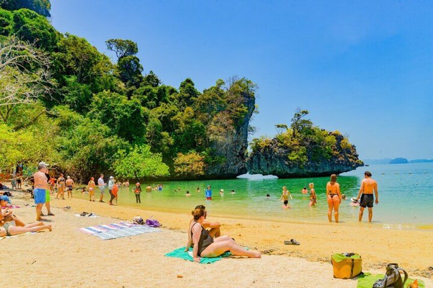 Una spiaggia con persone che prendono il sole e nuotano, circondata da vegetazione rigogliosa e acque cristalline. 1