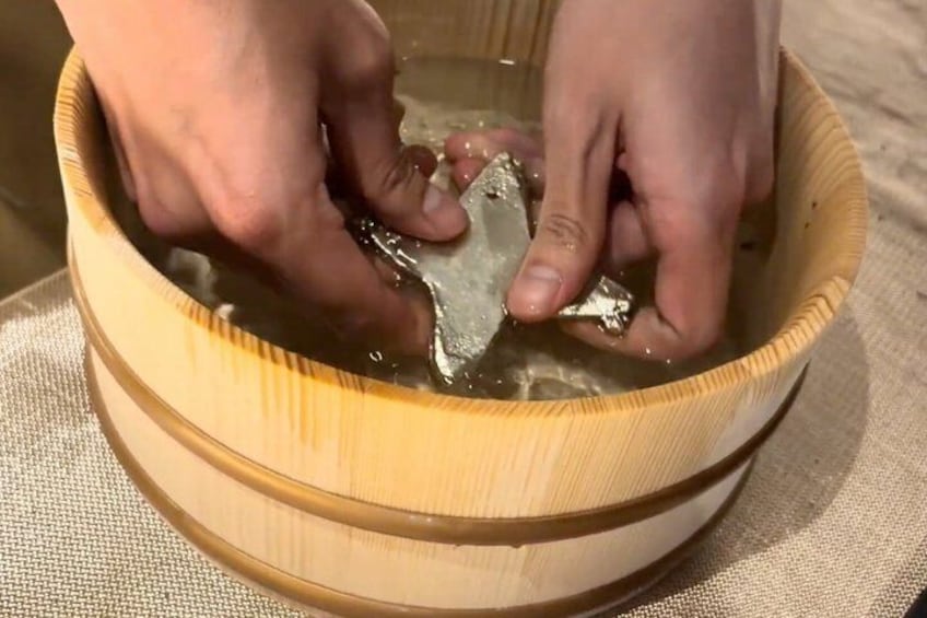 Hands holding a fish in a wooden bowl filled with water. 2
