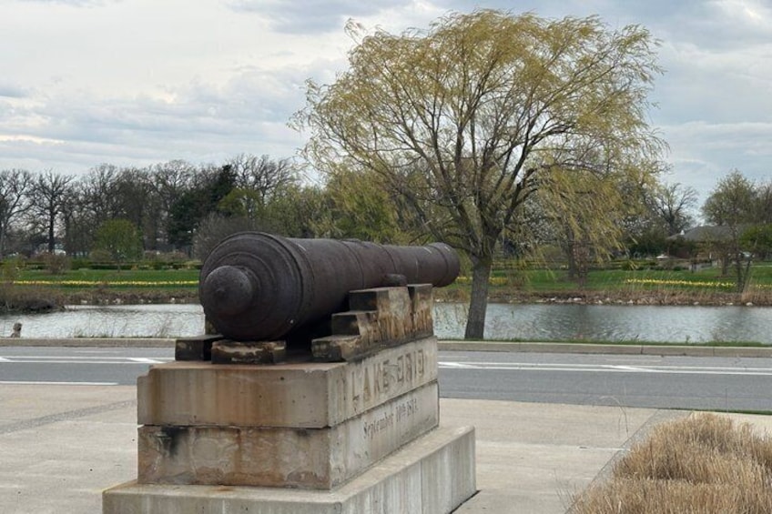 Un cañón sobre un pedestal de hormigón junto a una masa de agua, con árboles al fondo. 1