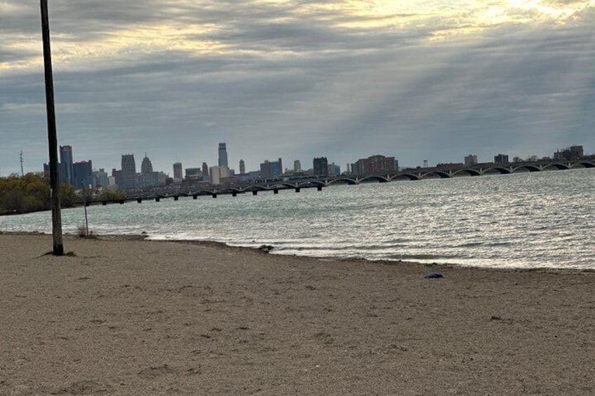 A river with a bridge, a city skyline in the background, and a sandy beach. 4