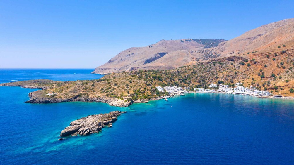 A coastal town with white buildings, clear blue waters, and a mountainous backdrop. 5
