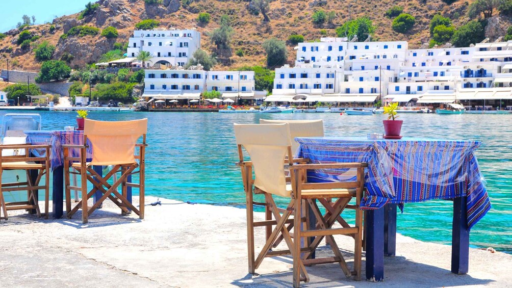 A seaside terrace with wooden chairs and tables, overlooking turquoise waters and white buildings with blue accents. 3