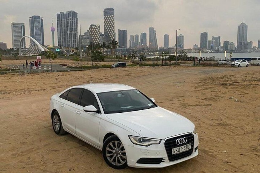A white car parked on a sandy area with a city skyline in the background. 1