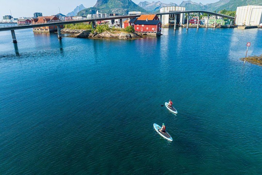 A bridge over a calm body of water with two people kayaking. 2