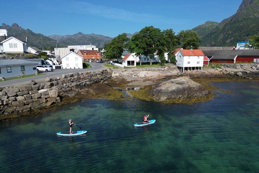 Two people paddleboarding on a calm body of water, surrounded by houses and mountains in the background. 5