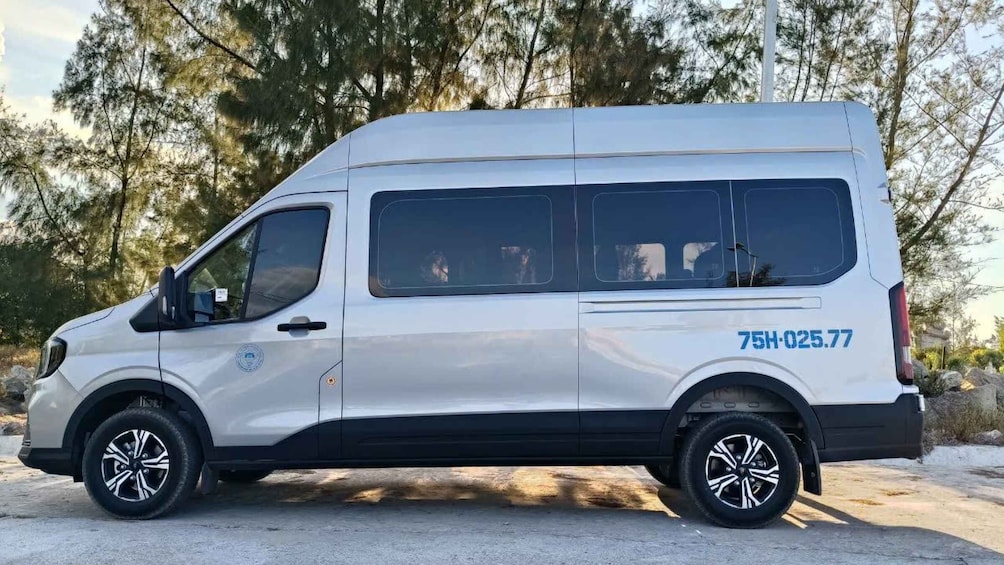 A white van parked on a paved surface with trees in the background. 1
