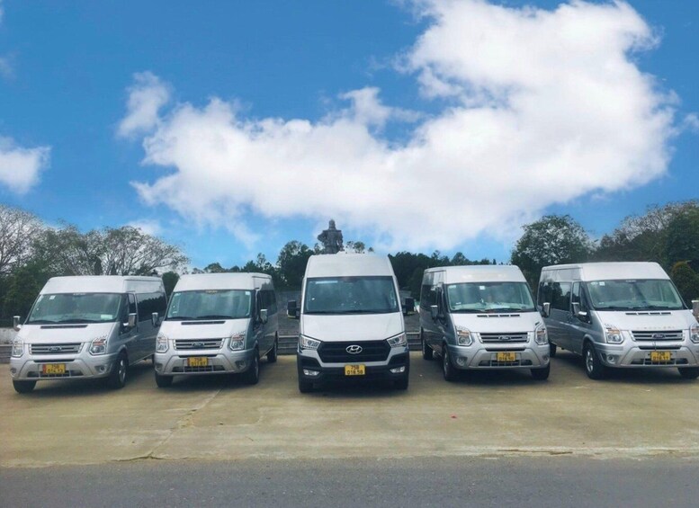 Five white vans parked in a row with a clear sky and trees in the background. 3