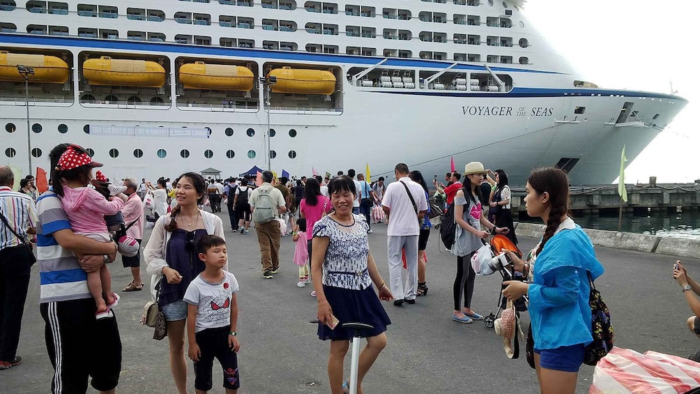 A large cruise ship named 'Voyager of the Seas' docked at a port with people walking around and taking photos. 4