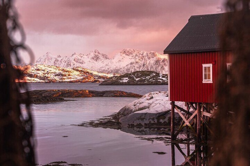 Una casa de madera roja sobre pilotes junto a un fiordo tranquilo, con montañas nevadas al fondo. 5