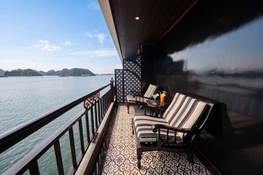 A balcony with striped chairs and a patterned floor, overlooking a body of water with distant land. 5
