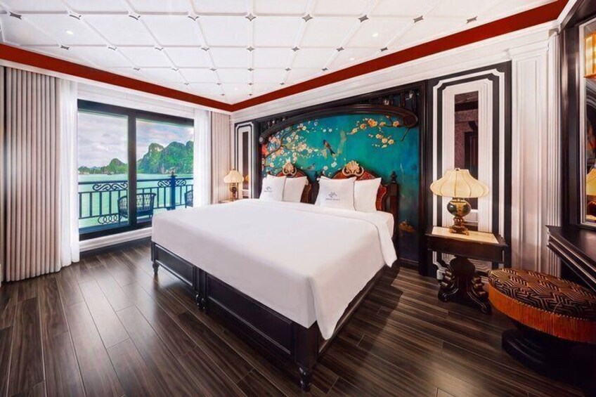 A large bed with white linens, a wooden floor, a balcony with curtains, and a decorative wall with floral patterns. 2