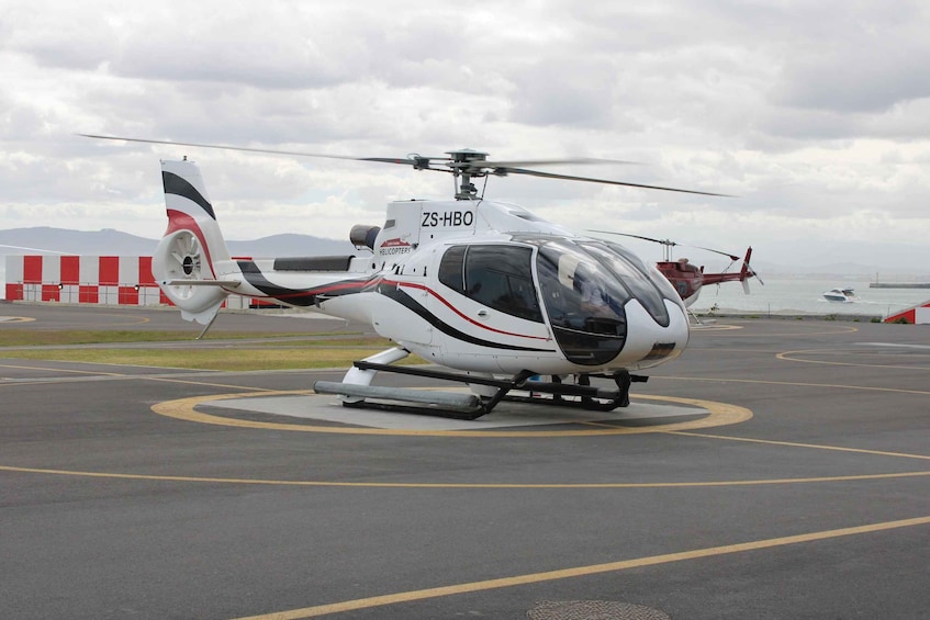 A white helicopter with red and black stripes on a tarmac with a mountainous backdrop. 4