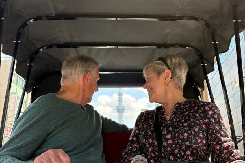 Twee personen in een voertuig, met een toren op de achtergrond. 3