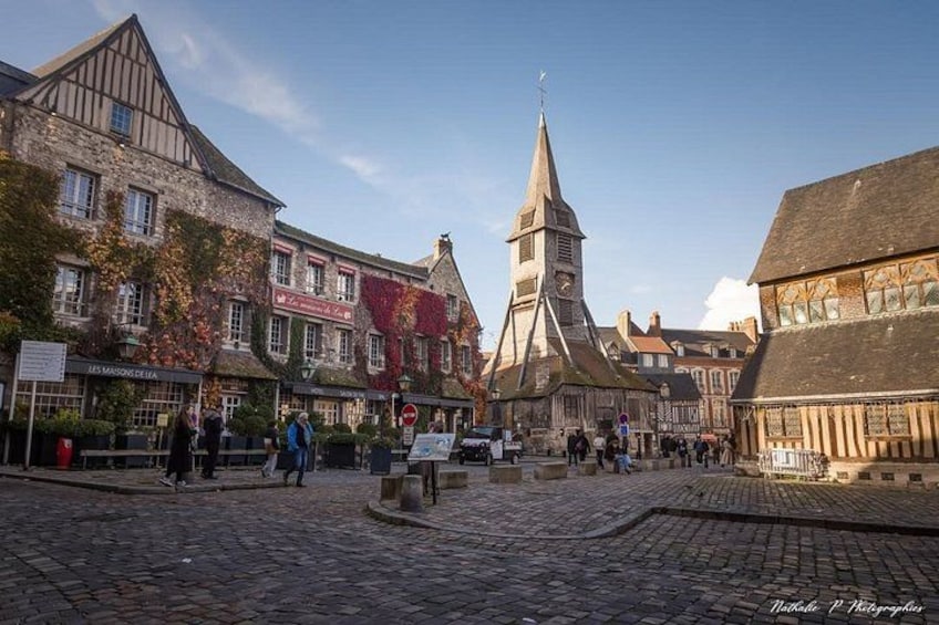 A cobblestone street with historic buildings, a church steeple, and pedestrians. 5