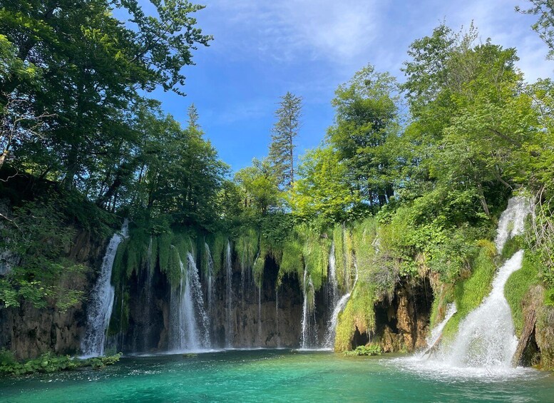 A multi-tiered waterfall surrounded by lush greenery and clear turquoise water. 4