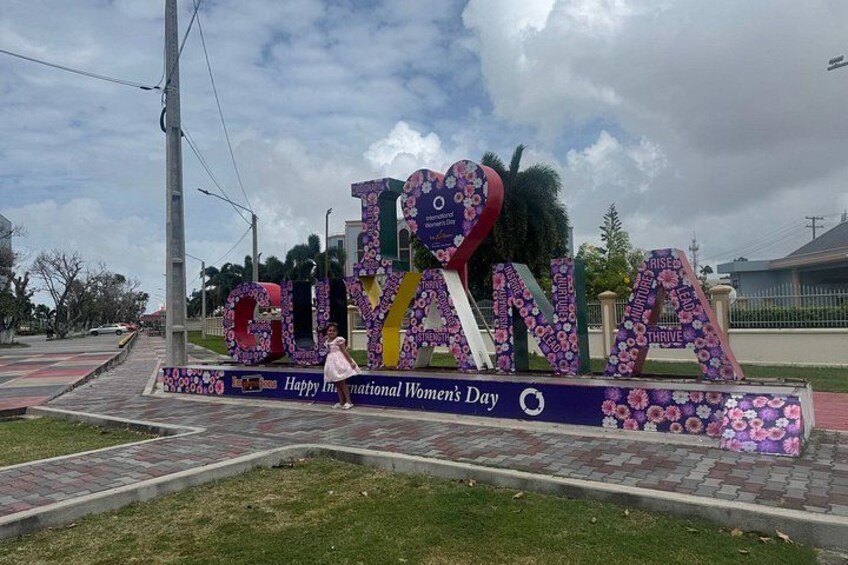 A large sign with the word 'GUYANA' and a message celebrating International Women's Day. 5
