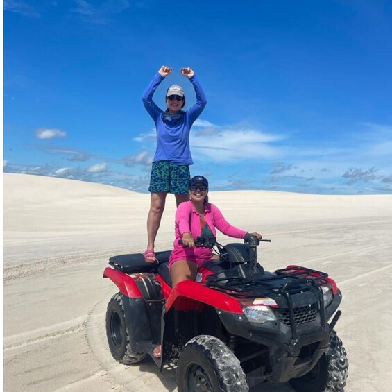 Two people on a red ATV in a desert with sand dunes. 5