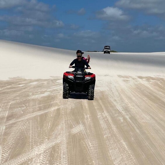 A person riding a red ATV on a sandy terrain with tire tracks, under a clear sky. 2