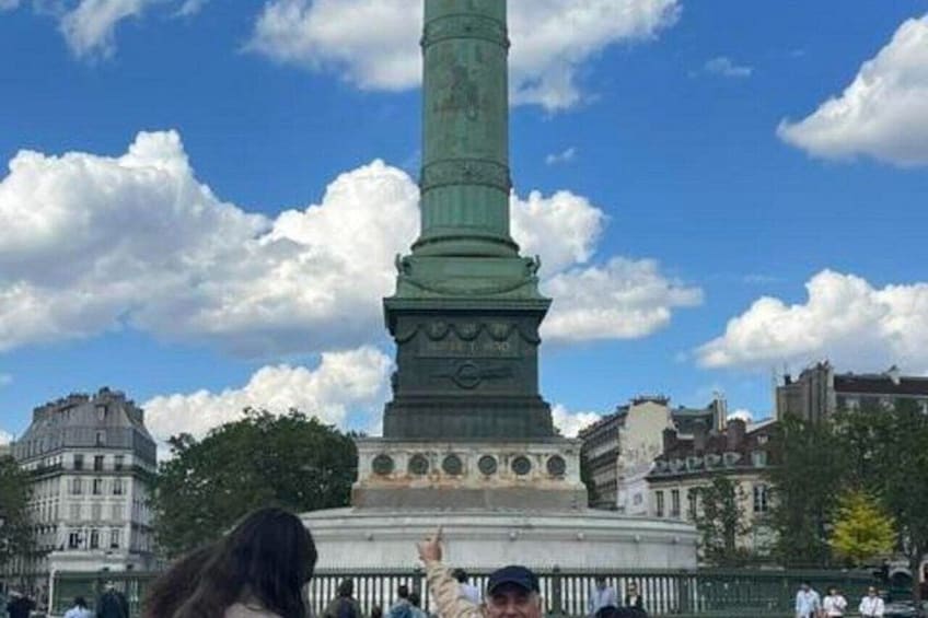 A green monument with a statue on top, surrounded by buildings and trees. 5