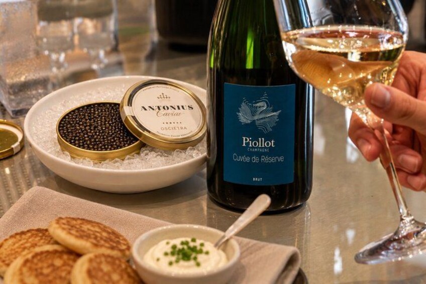 Een fles Piollot Cuvée de Reserva Brut champagne, pannenkoeken en een schaal saus op een tafel. 1