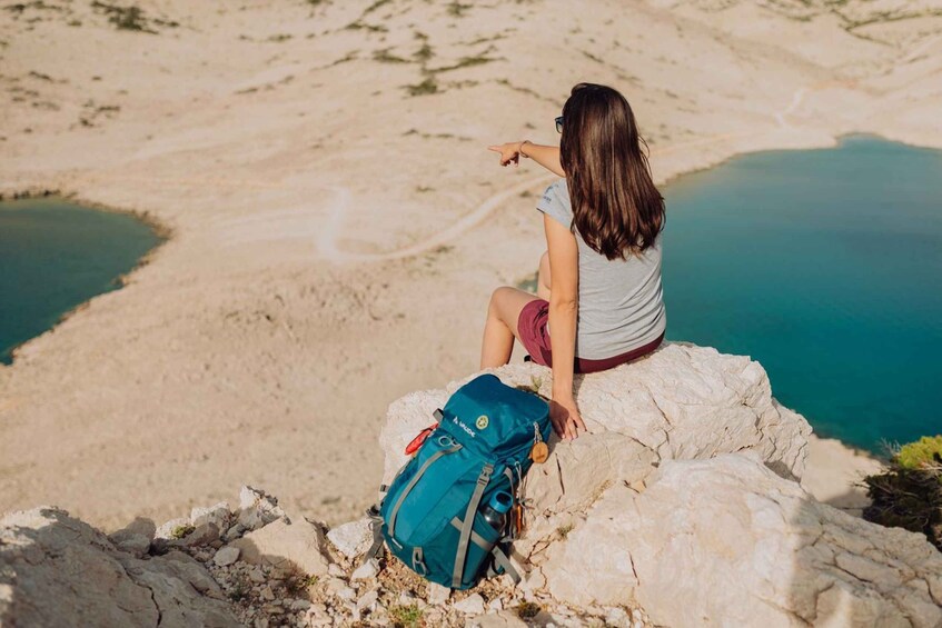 A person sitting on a rock with a backpack, overlooking a body of water and a mountainous landscape. 2