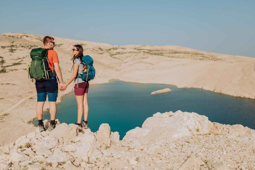 Two people hiking on rocky terrain with a body of water in the background. 3