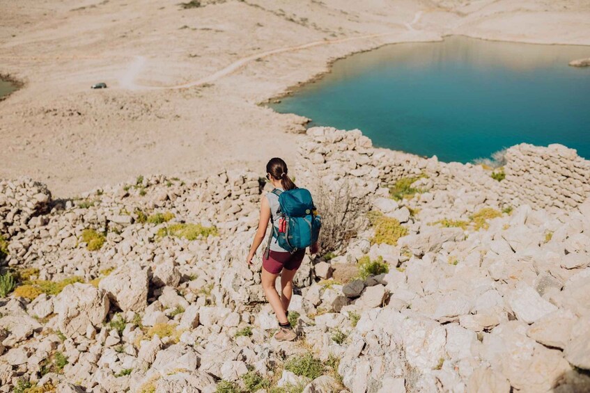 A hiker on a rocky trail with a backpack, a lake in the background, and sparse vegetation. 5