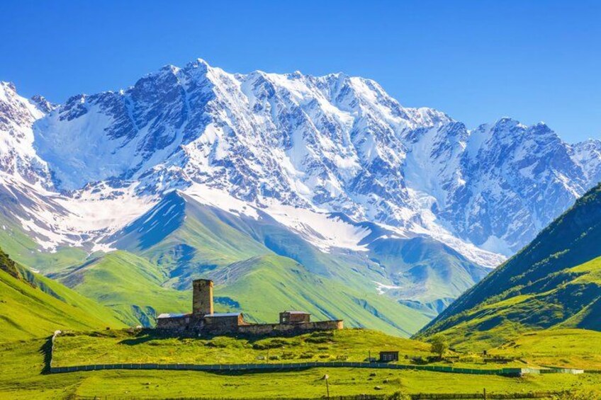 A mountainous landscape with a small stone structure in the foreground and snow-capped peaks in the background. 2