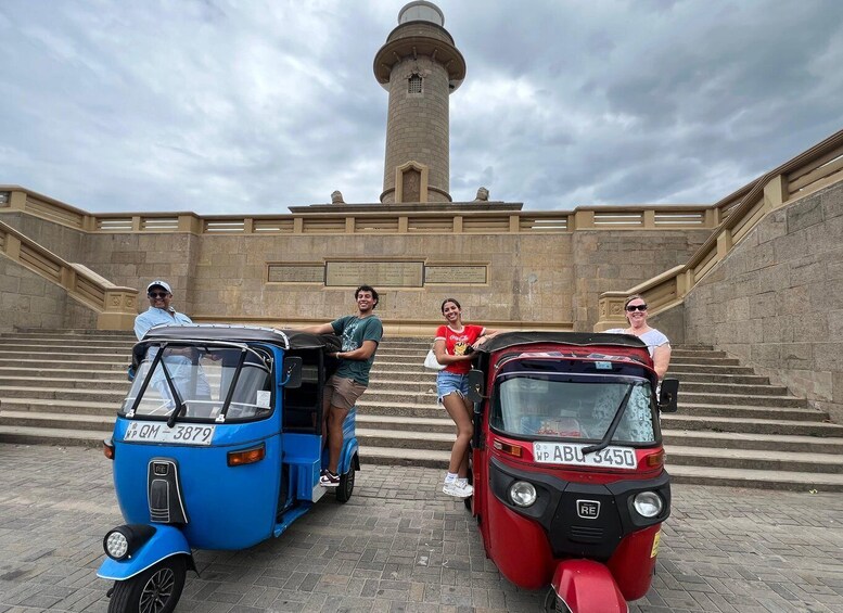 A blue and a red auto-rickshaw parked in front of a stone staircase leading to a tower. 4