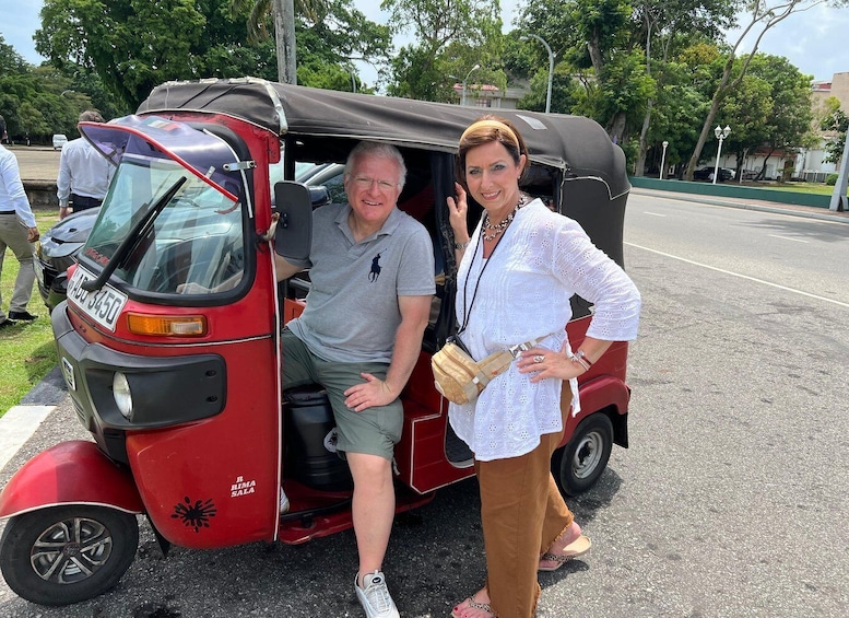 A red auto rickshaw with a black canopy, a man sitting inside, and a woman standing beside it. 3