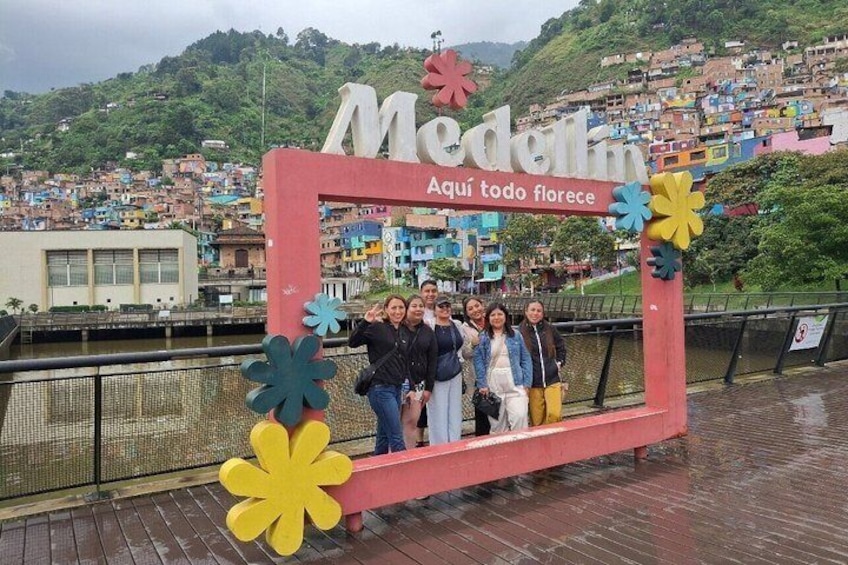 Un gruppo di persone che posa davanti a un cartello colorato con la scritta 'Medellin Aquí todo florece'. 2