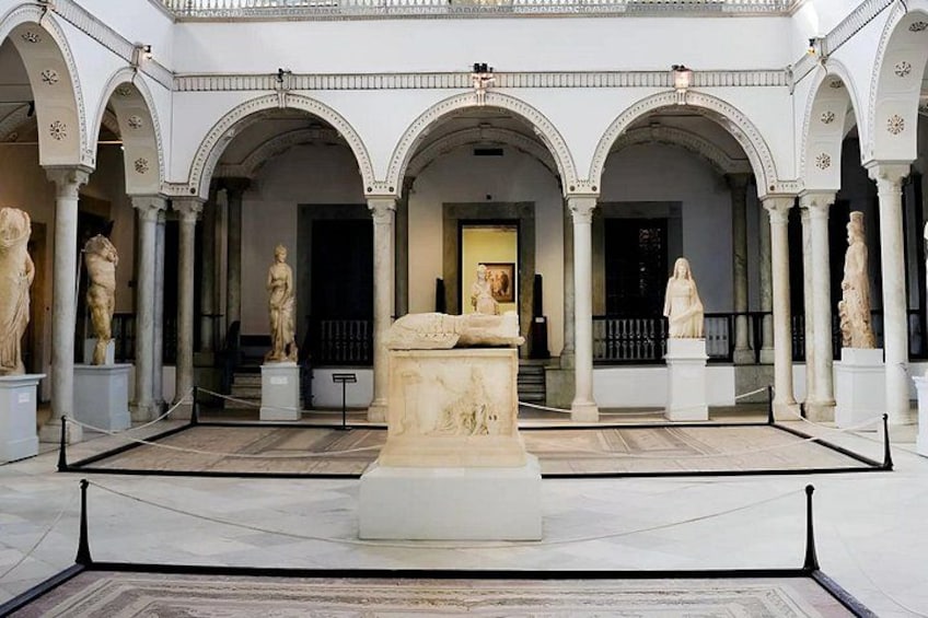 Ein klassischer Innenhof mit Bögen, Statuen und einer zentralen Skulptur. 2