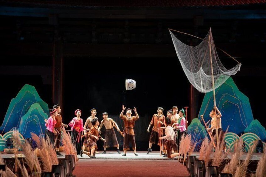 A stage with a group of people in traditional costumes, a large net, and a backdrop with geometric shapes. 1