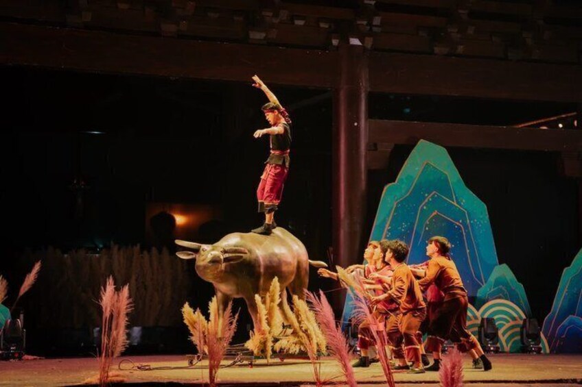 A performer balancing on a bull, with children in the background and decorative elements. 5