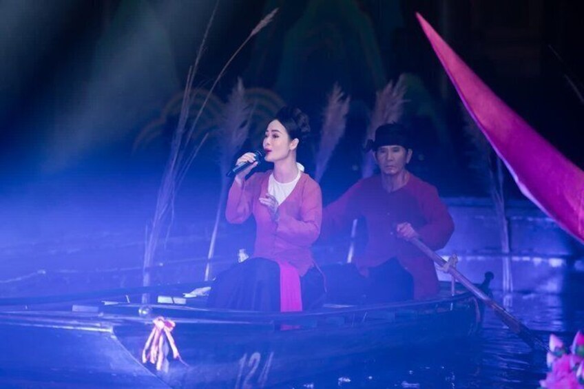 A person on stage with a microphone, another person in a red outfit, and a boat in the background. 2
