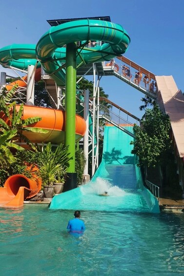 A water park with multiple slides, including a green spiral slide and an orange slide, and a person swimming in the water. 2