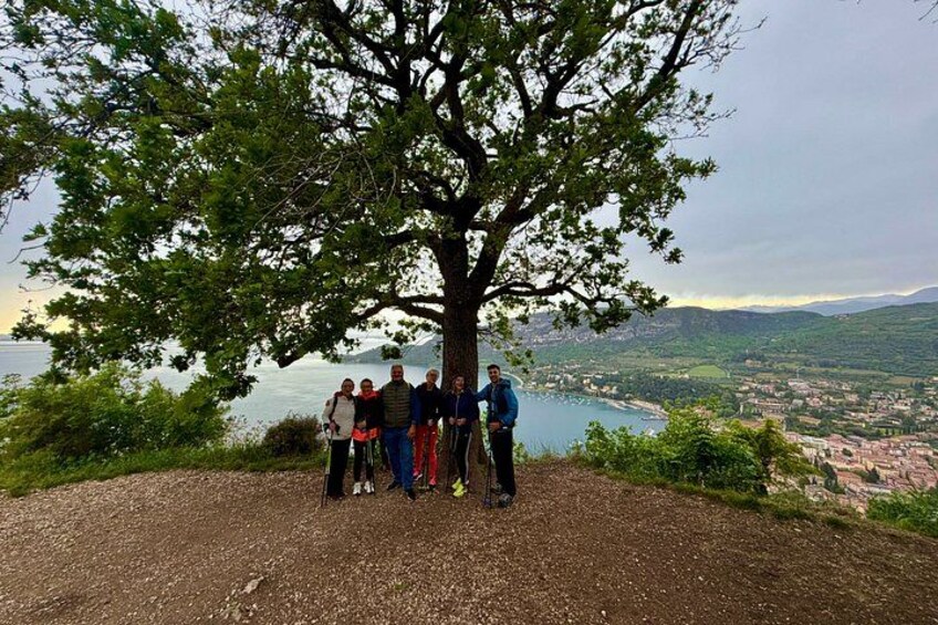 A group of people standing under a large tree with a scenic view of a lake and a town in the background. 2