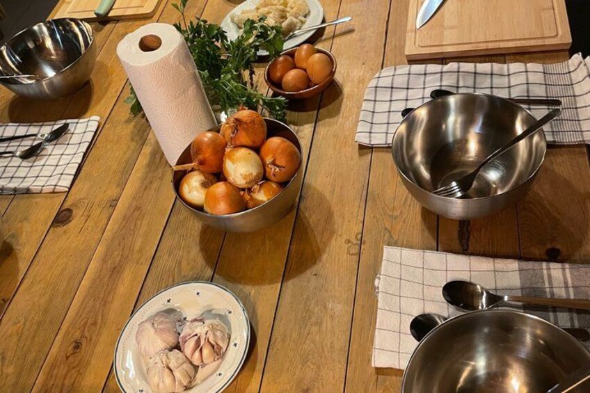Ein Holztisch mit verschiedenen Küchenutensilien, darunter Zwiebeln, eine Schüssel, ein Teller mit Hähnchen und Küchenpapier. 2