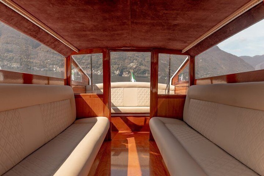 A boat interior with wooden paneling, cushioned seating, and a view of a mountainous landscape through large windows. 5