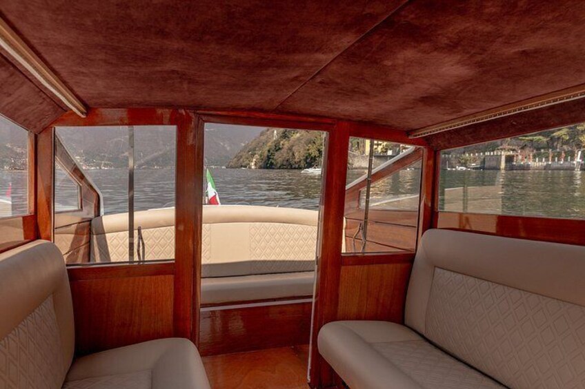 A boat interior with wooden panels, cushioned seats, and a view of a river with a bridge and greenery. 4