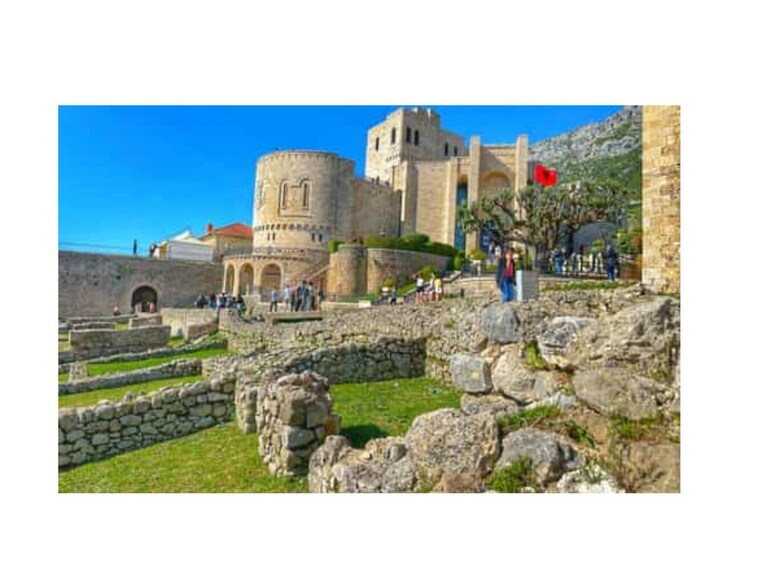 A historic stone fortress with a prominent tower, a red flag, and visitors. 5