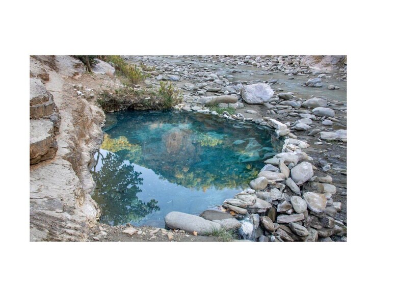 A natural pool surrounded by rocks and sparse vegetation. 3