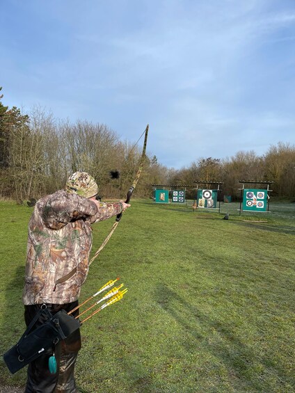 A person in camouflage attire aiming a bow at a target in an outdoor setting. 2