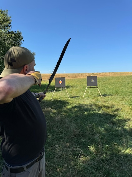 A person aiming a bow at two archery targets in an open field. 2