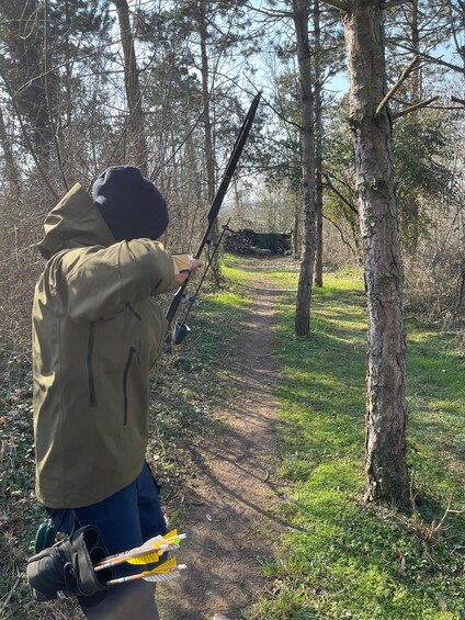 A person in a forested area aiming a bow and arrow. 3